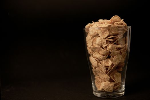 cornflakes in a transparent glass against a black background with place for text