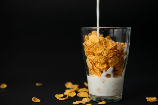 cornflakes with milk in a transparent glass against a black background with place for text