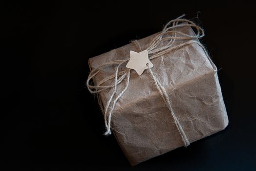 Gift box in craft paper on black background with star in center for text or logo. Empty place for text