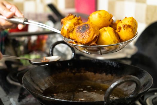 Shallow depth of feild shot of vada potatoes wrapped in flour being taken out of hot oil after deep frying . This popular street food is very popular in mumbai India a breakfast for many as the market opens up