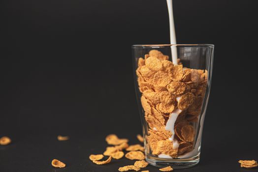 cornflakes with milk in a transparent glass against a black background with place for text