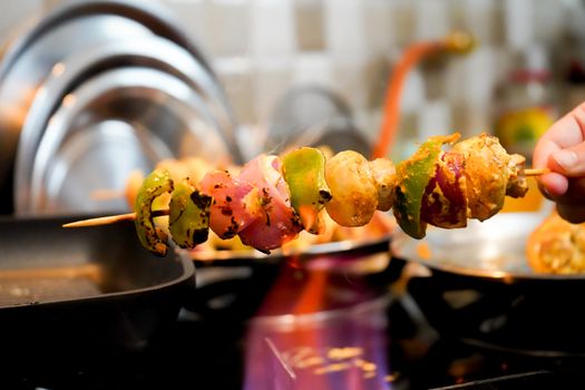 Macro selective focus shot of cottage cheese, onions, mushrooms and more on a wooden skewer roasted over an open flame to char it. Shows home cooking of indian paneer tikka masala a tasty spicy street food with charred vegetables