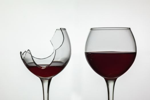 Broken and not broken wine glass with red wine on white background.