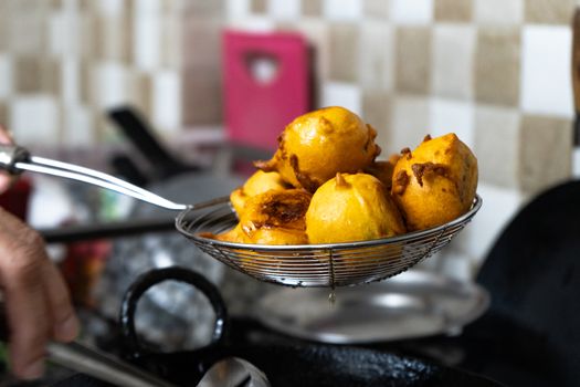 Shallow depth of feild shot of vada potatoes wrapped in flour being taken out of hot oil after deep frying . This popular street food is very popular in mumbai India a breakfast for many as the market opens up