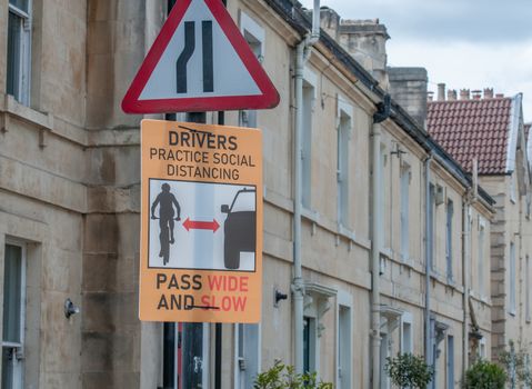 sign issuing warning to drivers about pedestrians stepping into the road to maintain social distancing