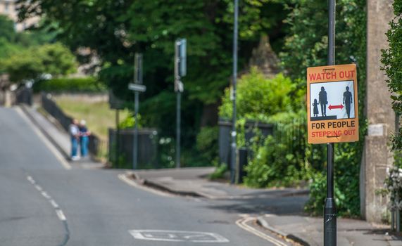 sign issuing warning to drivers about pedestrians stepping into the road to maintain social distancing