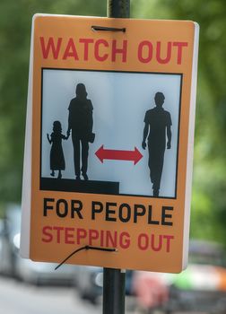 sign issuing warning to drivers about pedestrians stepping into the road to maintain social distancing