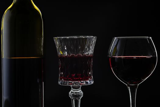 Wine. Red wine in two wine glasses over dark background. Silhouette of bottle with rose wine