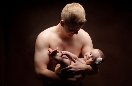 Male holding nice infant baby girl. Daughter on father's arms. Human growth and development. New generation. Cheerful man and his baby. New life concept. Dark background