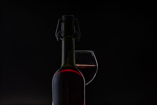 Wine. Red wine in wine glass over dark background. Silhouette of bottle with rose wine and opener on cork