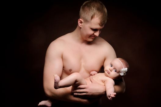 Male holding nice infant baby girl. Daughter on father's arms. Human growth and development. New generation. Cheerful man and his baby. New life concept. Dark background