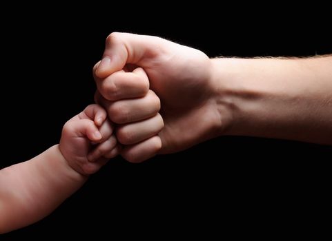 The hands of the child and the father. The fists are together. Black background.