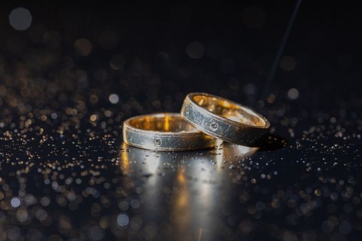 Wedding rings lying on dark surface shining with light close up macro. Water splashes