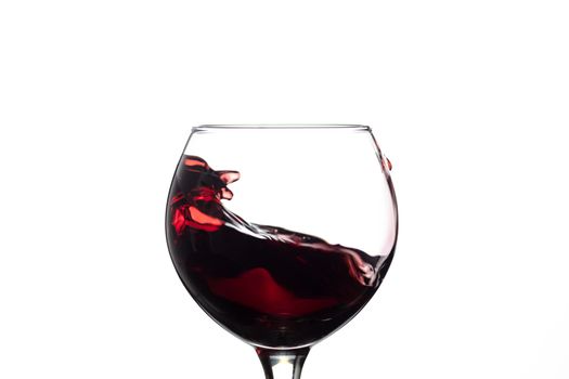Red wine splash into glass on white background.