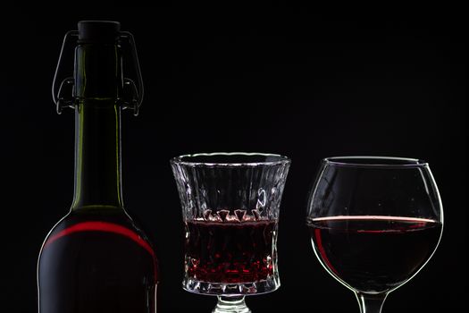Wine. Red wine in two wine glasses over dark background. Silhouette of bottle with rose wine and opener on cork