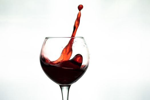 Red wine splash into glass on white background.