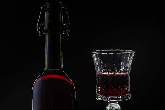 Wine. Red wine in wine glass over dark background. Silhouette of bottle with rose wine and opener on cork