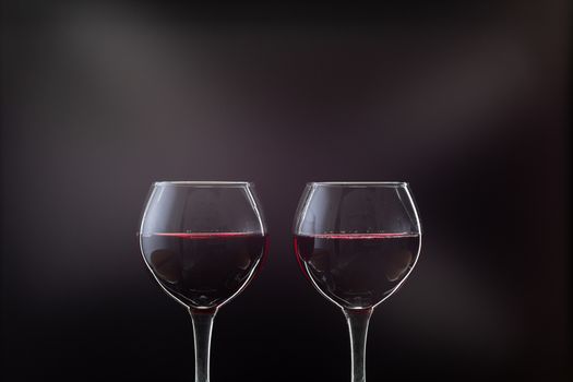 Rose wine. Red wine in two wine glasses over dark background with rays of light.