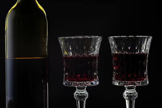 Wine. Red wine in two wine glasses over dark background. Silhouette of bottle with rose wine