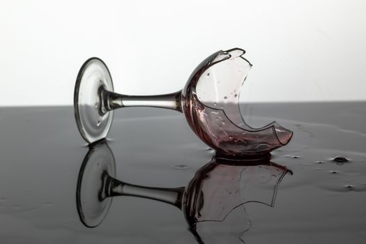 Broken wine glass with red wine which is laying on the wet surface. White background