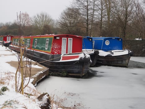 Colorful canal boats moored in icy water during winter snow, Kennet and Avon Canal, Aldermaston, Berkshire, UK