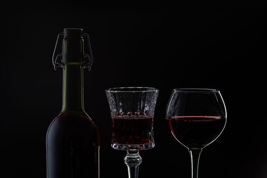 Wine. Red wine in two wine glasses over dark background. Silhouette of bottle with rose wine and opener on cork