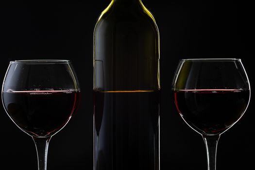 Wine. Red wine in two wine glasses over dark background. Silhouette of bottle with rose wine