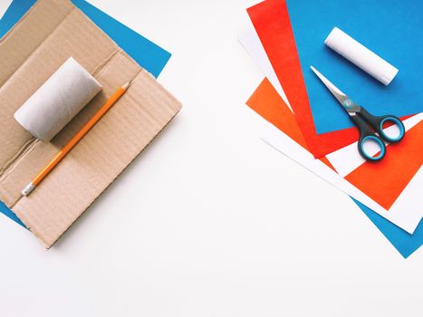 Top view on table with colored paper, glue, scissors, pencil and carton core of toilet paper. Tools for making eco-friendly toys. Reuse of tissue paper rolls.