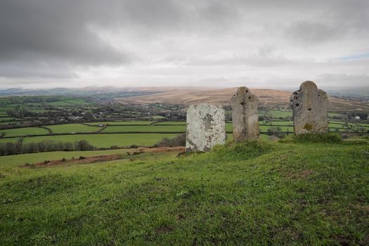 Gravestones at the 13th century church of St Michael de Rupe on top of Brent Tor looking out across the clouds rolling in over the distant hills, Dartmoor National Park, Devon, UK