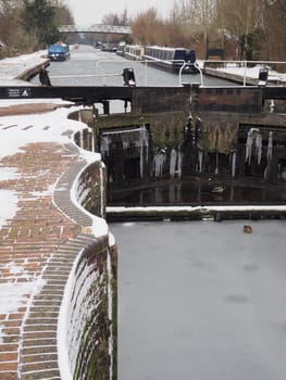 Ducks on the frozen ice in the bottom of the historic Aldermaston Lock in winter with icicles on the lock gates and canal boats and footbridge in the distance, Kennet and Avon Canal, Berkshire, UK