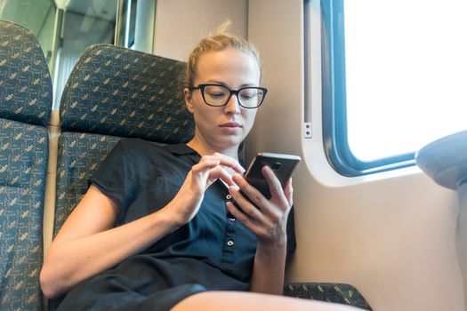 Caucasian female traveler using mobile phone applications while traveling by train.