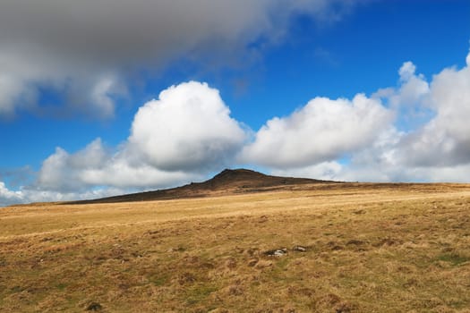 Hare Tor stands isolated against billowing white cumulus clouds in a blue sky overhead, Dartmoor National Park, Devon, UK