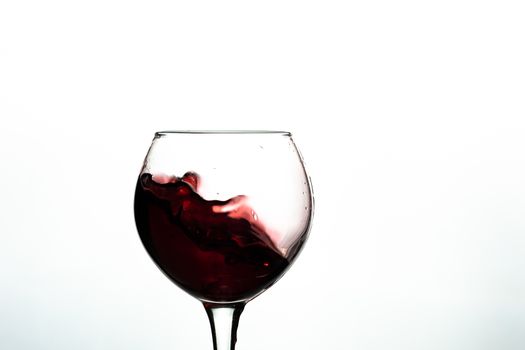 Red wine splash into glass on white background.