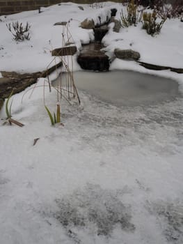 Garden pond with stream and waterfall in winter with snow and frozen ice on the water