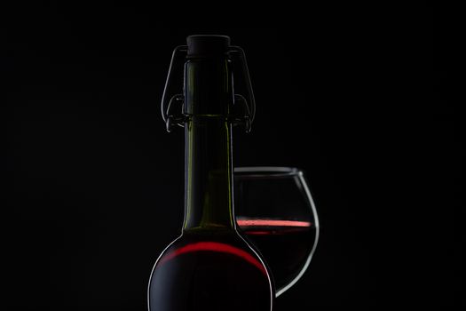 Wine. Red wine in wine glass over dark background. Silhouette of bottle with rose wine and opener on cork