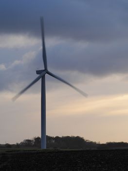 A wind turbine spinning quickly on a windy day set against a stormy and overcast evening sky