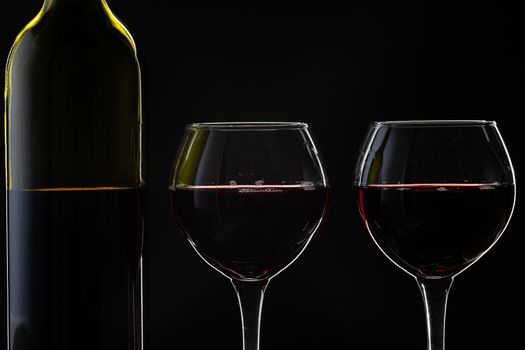 Wine. Red wine in two wine glasses over dark background. Silhouette of bottle with rose wine