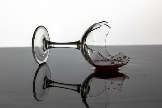 Broken wine glass with red wine which is laying on the wet surface. White background