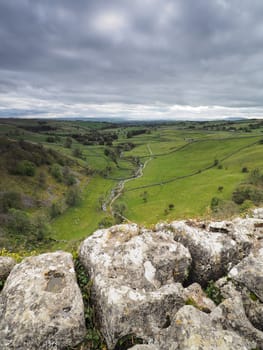 The fissured limestone pavement above Malham Cove overlooking the valley of Malham Beck set against a moody overcast sky, Yorkshire Dales, UK
