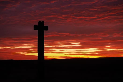 Silhouette of Young Ralph Cross, a wayside stone cross, set against a magnificent sunset lighting up the clouds yellow, orange and red, Westerdale, North York Moors National Park, UK