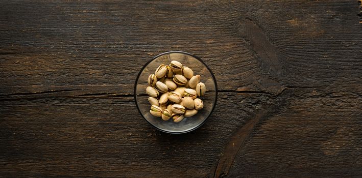 Pistachios in a small plate on a vintage wooden table. Pistachio is a healthy vegetarian protein nutritious food. Natural nuts snacks