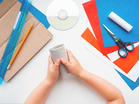 Child makes eco-friendly toy of colored paper and used toilet paper core. Also he needs carton, scissors, glue, CD-disk, pencil and ruler. Reuse tissue rolls. Making toys from improvised materials.