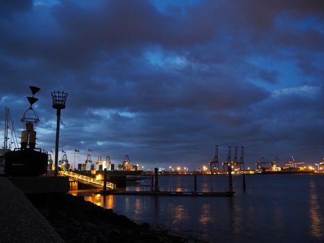 Port of Felixstowe at night with cranes and container ships lit up on a calm sea against a cloudy sky taken from Shotley Point, Suffolk, UK