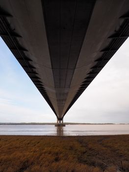 Looking out over the river underneath the road deck of Humber Bridge, a single span suspension bridge, viewed from Barton-on-Humber, Lincolnshire looking back towards Hessle, Yorkshire, UK