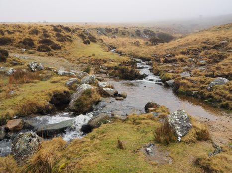 Footpath across Red-a-ven Brook as it cascades over rocks high up on the moor and just below the mist and low cloud, Dartmoor National Park, Devon, UK