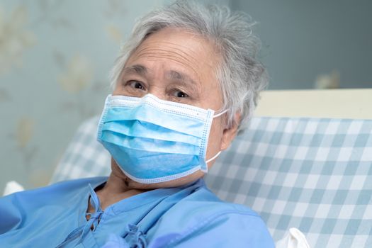 Asian senior or elderly old lady woman patient wearing a face mask to protect coronavirus and while sitting on bed in nursing hospital ward : healthy strong medical concept