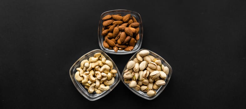 Almond, pistachio and cashew in a small plates which standing on a black table. Nuts is a healthy vegetarian protein and nutritious food