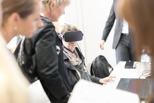 Unrecognizable woman wearing virtual reality headset glasses on virtual reality trade show business conference presentation.