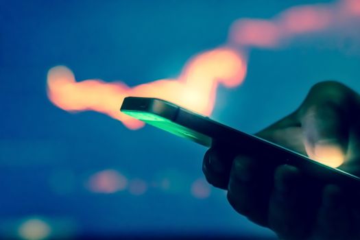 Trader in dark using mobile phone against stock market charts