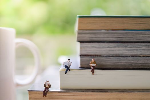 Business, Information and social distancing concept. Group of businessman miniature figure sitting and reading newspaper and book on stack of books with mug cup of hot coffee.